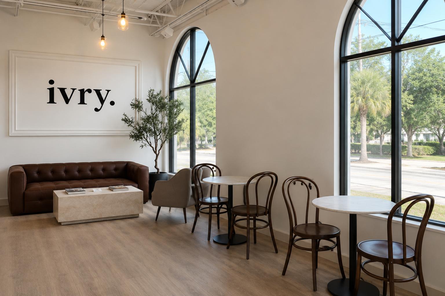 The seating room at ivry. — the wall logo and leather sofa beside marble tables under two arched windows.