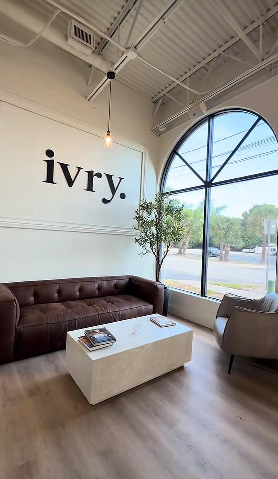 Inside ivry. — a tufted brown leather sofa and pale stone coffee table beside a tall arched window looking onto the South Tampa street.